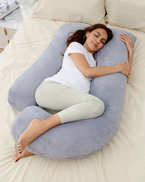 Pregnant woman resting on a U-shaped maternity pillow for comfortable sleep and body support, light gray plush material.